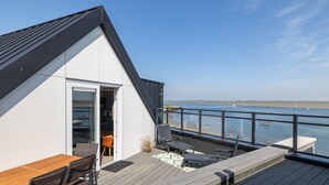 Een modern terras met uitzicht op zee, een houten tafel en stoelen.