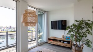 Een moderne woonkamer met een groot raam, een flatscreen televisie, een houten console tafel en een potplant.