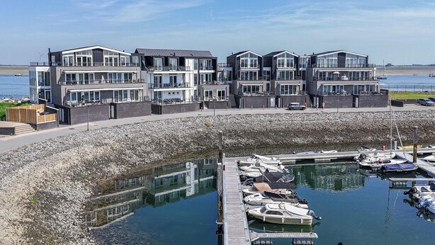 Een pand aan het water met moderne architectuur, voorzien van meerdere balkons en grote ramen.