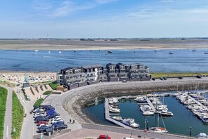 A marina with boats docked, a parking area, and a beach with people.