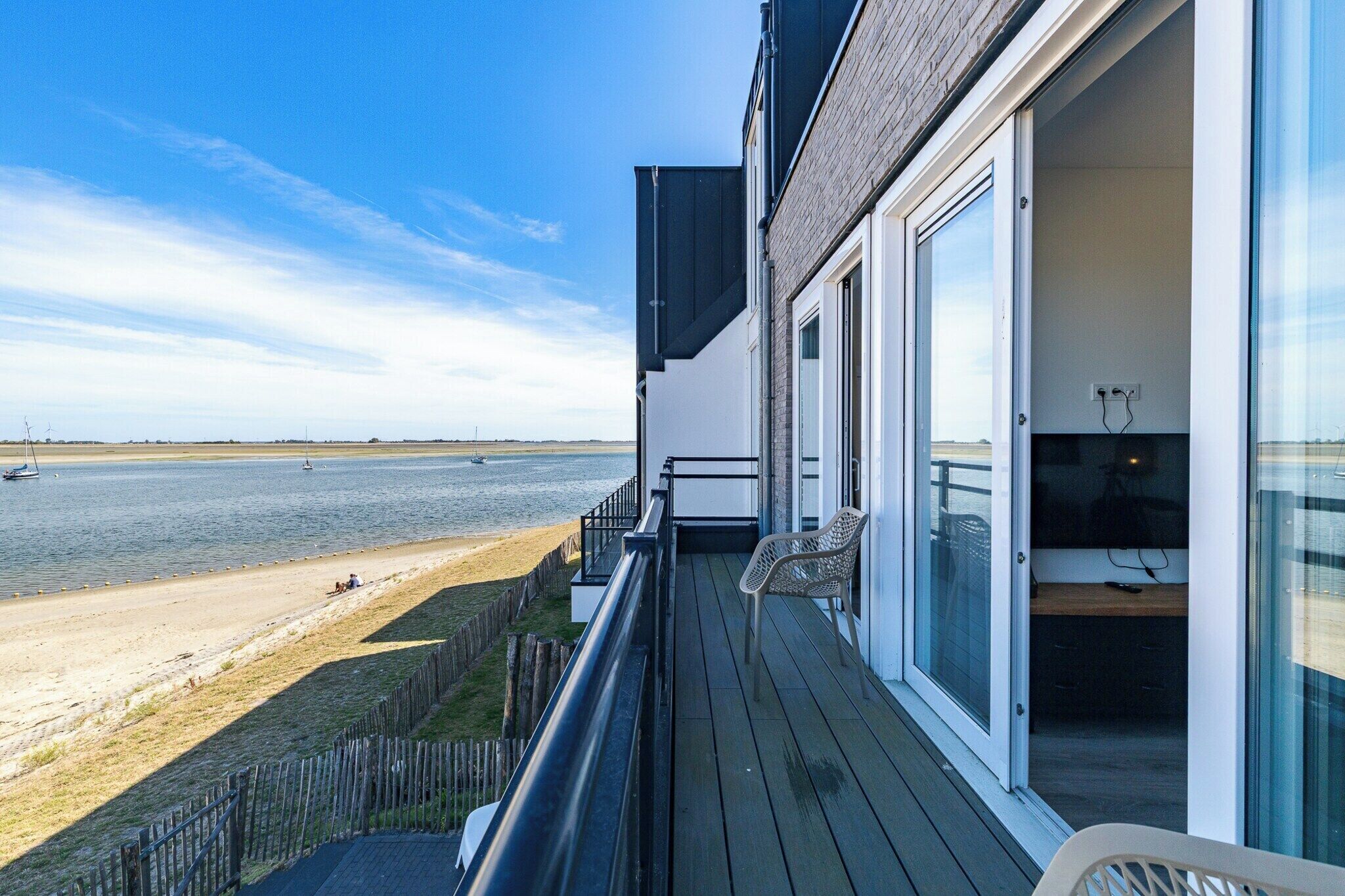 Een balkon met uitzicht op zee, een houten terras en een glazen deur die leidt naar een kamer met een televisie.