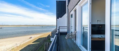 A balcony with a view of the sea, a wooden deck, and a glass door leading to a room with a TV.