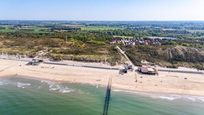 Vista aérea de uma área costeira com praia, um píer e um conjunto de edifícios.