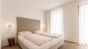 A neatly made double bed with a patterned headboard, bedside lamps, and a wooden nightstand.