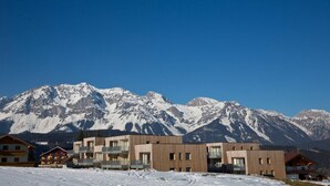 A modern hotel with multiple floors and balconies, set against a backdrop of snow-covered mountains. - Lush apartment with private sauna (Schladming - Rohrmoos)