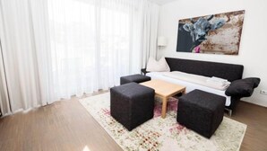 A modern living room with a sofa, two black ottomans, a coffee table, and a painting on the wall. - Lush apartment with private sauna (Schladming - Rohrmoos)