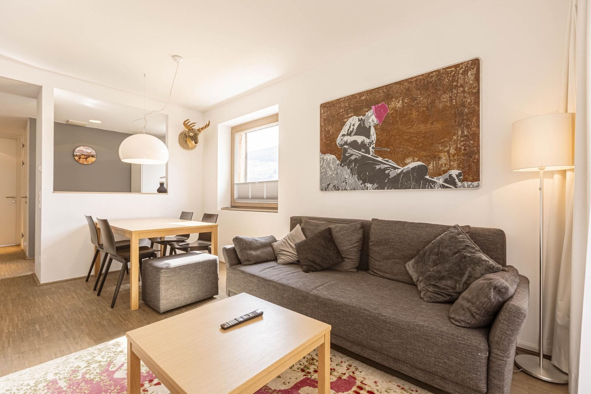 Uma sala de estar moderna com um sofá cinzento, uma mesa de centro de madeira e um espaço de jantar com mesa e cadeiras.