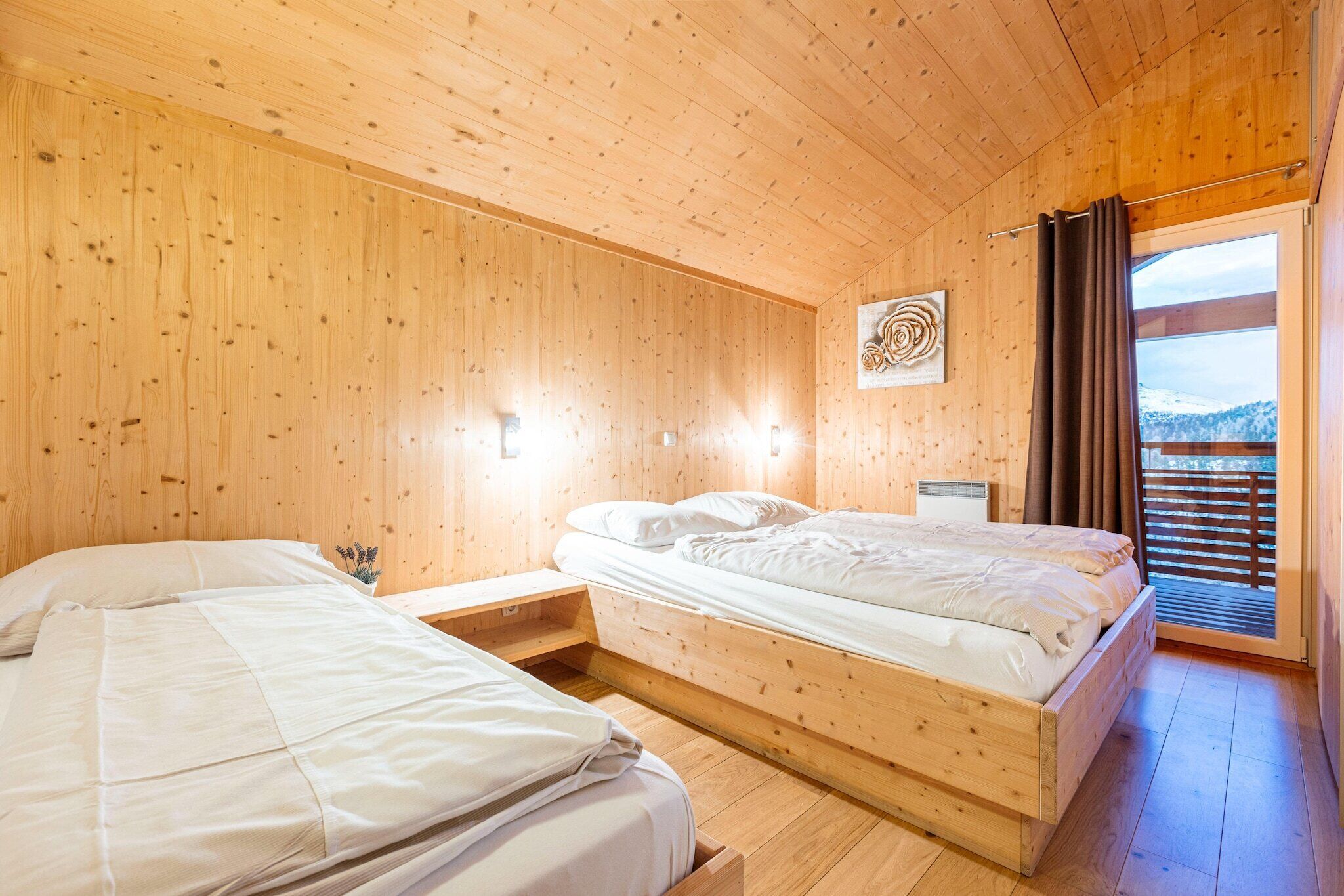 A wooden cabin bedroom with two beds, a window with curtains, and a wall-mounted light fixture.