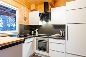 Et moderne køkken med hvide skabe, en ovn i rustfrit stål og et vindue med udsigt til en skov.