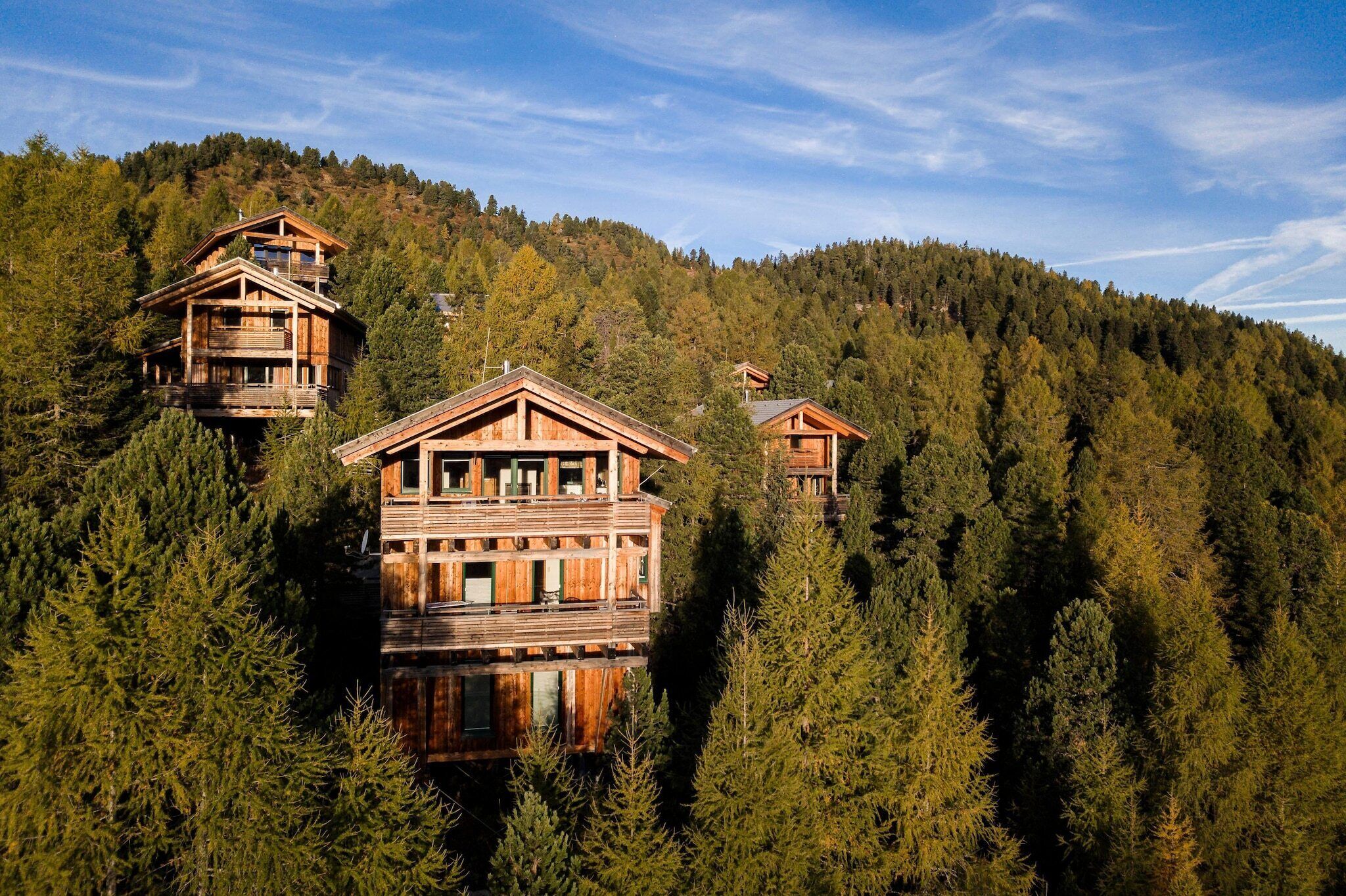 Un ensemble de chalets en bois à plusieurs niveaux, entouré d’une forêt dense sur le flanc d’une colline.