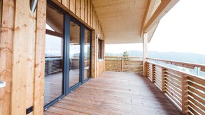 Une terrasse en bois avec des portes vitrées donnant sur un balcon, d’où l’on peut admirer un paysage montagneux.