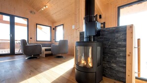 L’intérieur chaleureux d’un chalet avec un poêle à bois, deux fauteuils gris et un mur décoratif en pierre.
