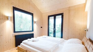 Une chambre dans une cabane en bois, avec deux lits, de grandes fenêtres et une vue sur les arbres.