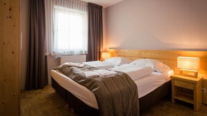 A double bed with a wooden headboard, a bedside table with a lamp, a window with curtains, and a radiator.