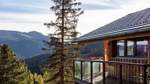 A wooden cabin with a glass balcony overlooking a mountainous landscape.