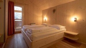 Quarto de madeira com uma cama, mesa de cabeceira e luminária na parede.
