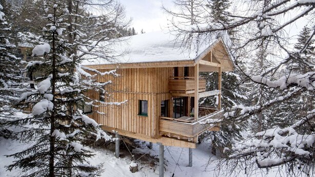 Uma cabana de madeira com varanda, rodeada por árvores cobertas de neve.