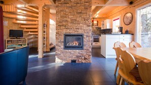 Eine moderne Küche mit Kamin aus Stein, Holzbalken und einem Essbereich mit großem Tisch und Stühlen.