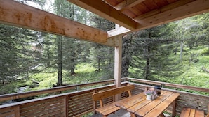 Eine Holzterrasse mit Tisch und Bänken mit Blick auf ein bewaldetes Gebiet.