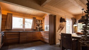 A wooden cabin interior with a kitchen, dining area, and large windows.