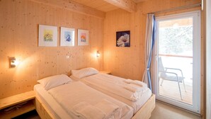 A wooden-paneled room with two beds, a sliding glass door to a balcony, and wall-mounted artwork. - Lovely chalet with sauna (Turracherhöhe)