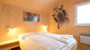 Une pièce de cabane en bois avec deux lits, un tapis en fourrure accroché au mur, un tableau et une fenêtre.