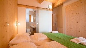 Een kamer met twee bedden, een groene spreidek, een houten garderobe, en een badkamer met een wastafel en spiegel.