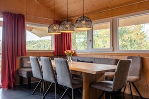 A wooden interior with a long table, cushioned seating, and large windows. - Chalet near Ski Resort in Austria with Sauna (Turracherhöhe)