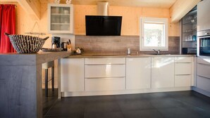 A modern kitchen with a central island, white cabinetry, a black range hood, and a window providing natural light. - Chalet near Ski Resort in Austria with Sauna (Turracherhöhe)