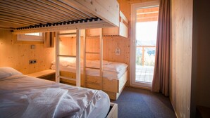 A wooden cabin room with bunk beds, a window, and a door leading to an outdoor balcony. - Chalet near Ski Resort in Austria with Sauna (Turracherhöhe)