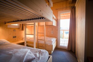 Quarto de cabana de madeira com beliches, uma janela e porta que dá para uma varanda externa.
