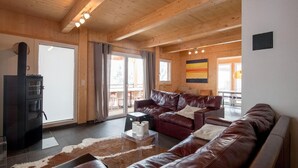 A spacious living room with a wooden ceiling, leather sofas, a glass coffee table, and a fireplace. - Chalet in Austria near Ski Resort (Turracherhöhe)