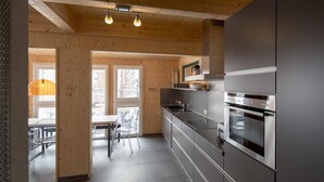 A modern kitchen with stainless steel appliances, wooden beams, and a dining area with clear chairs. - Chalet in Austria near Ski Resort (Turracherhöhe)
