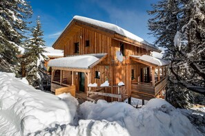 A wooden cabin with a covered porch and a snow-covered roof, surrounded by snow-laden trees. - Chalet in Alps with Sauna near Ski Slopes (Turracherhöhe)