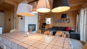 L’intérieur d’un chalet chaleureux, avec une table à manger, des chaises, un canapé et un téléviseur.