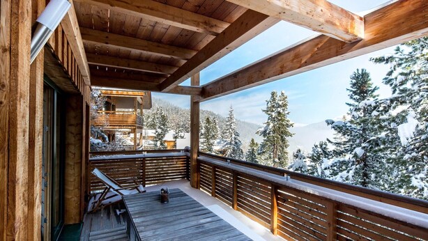 Une terrasse en bois offrant une vue sur des arbres et des montagnes enneigés.