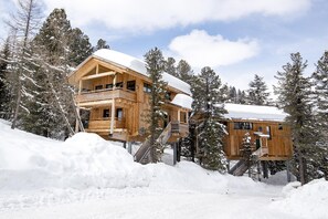 Une cabane en bois dotée d’un balcon, entourée d’arbres couverts de neige.