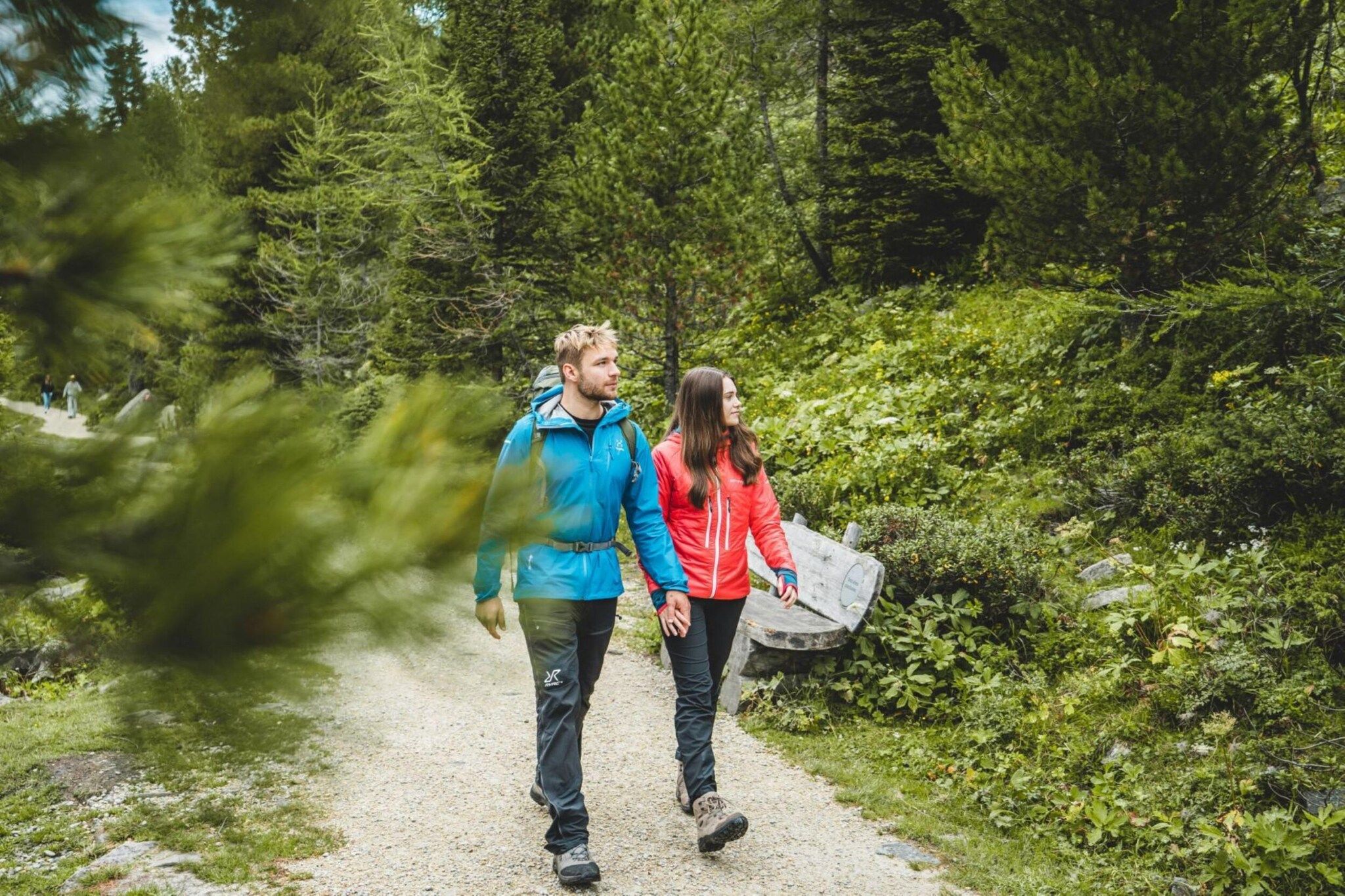 Two people walking on a gravel path surrounded by dense greenery.