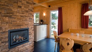 A cozy room with a fireplace, wooden walls, a dining area, and a view of the outdoors. - Amazing chalet with infrared sauna (Turracherhöhe)