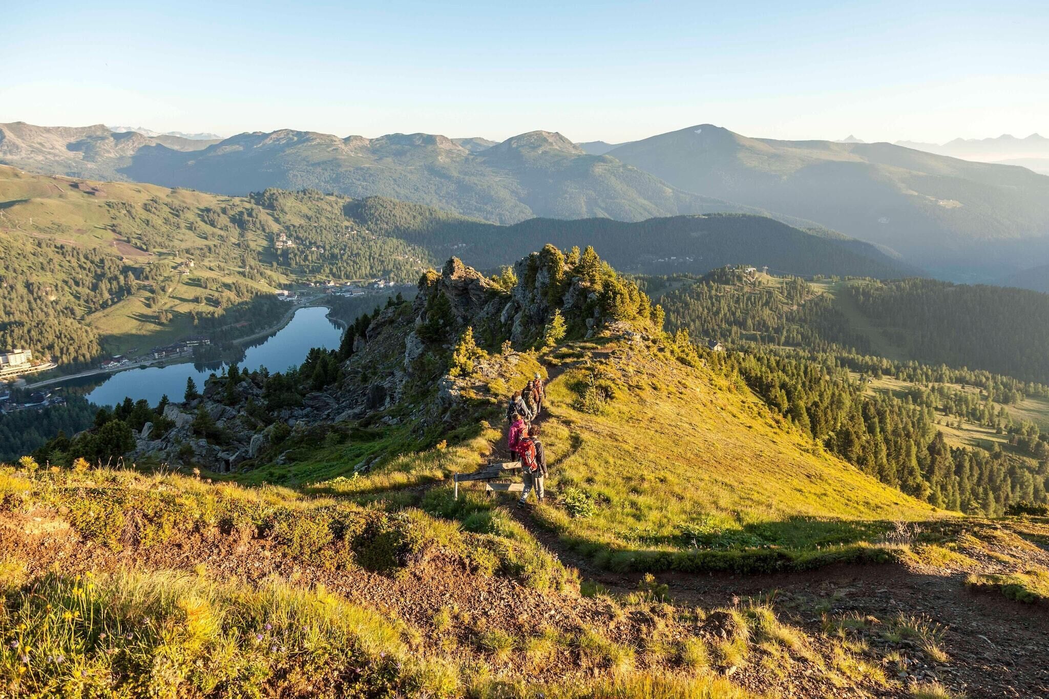 Un paysage montagneux avec un lac, un sentier de randonnée et un petit village situé dans la vallée.