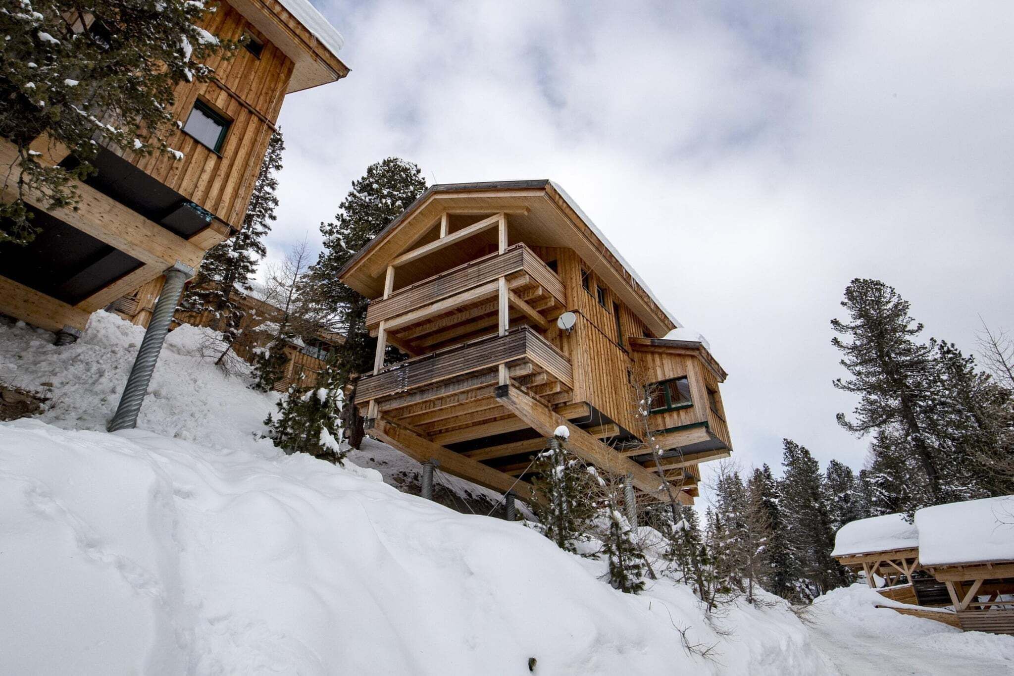 Una cabaña de madera con balcón, rodeada de nieve y árboles.