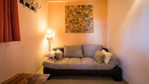 A cozy room with a wooden wall, a patterned artwork, a sofa with cushions, and a small table. - Cosy chalet with infrared sauna (Turracherhöhe)