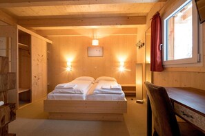 A wooden room with a bed, two wall-mounted lights, a window with a curtain, and a wooden desk.