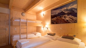 A wooden cabin room with bunk beds, a painting of a mountain, and a wooden door. - Cosy chalet with infrared sauna (Turracherhöhe)