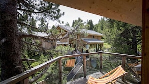 A wooden deck with a hammock and a view of a cabin surrounded by trees. - Cosy chalet with infrared sauna (Turracherhöhe)