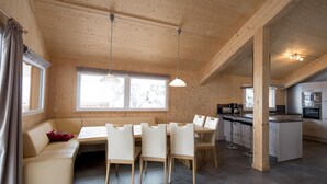 Ett modernt kök med träskåp och en köksö, en matplats med bord och stolar samt en mysig sittgrupp med en soffa och kuddar.