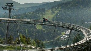 A chairlift with a person seated, surrounded by a mountainous landscape and a winding road. - Apartment in Pine Forest near Ski Slopes (Turracherhöhe)