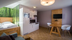 A modern room with a bed, a kitchenette, a dining table, and a TV mounted on a wooden wall. - Apartment in Pine Forest near Ski Slopes (Turracherhöhe)