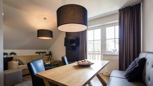 A modern living room with a wooden dining table, black chairs, a sofa, and a large window with curtains.