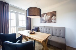 Un salon moderne avec une table à manger en bois, un canapé gris et une grande fenêtre avec des rideaux.